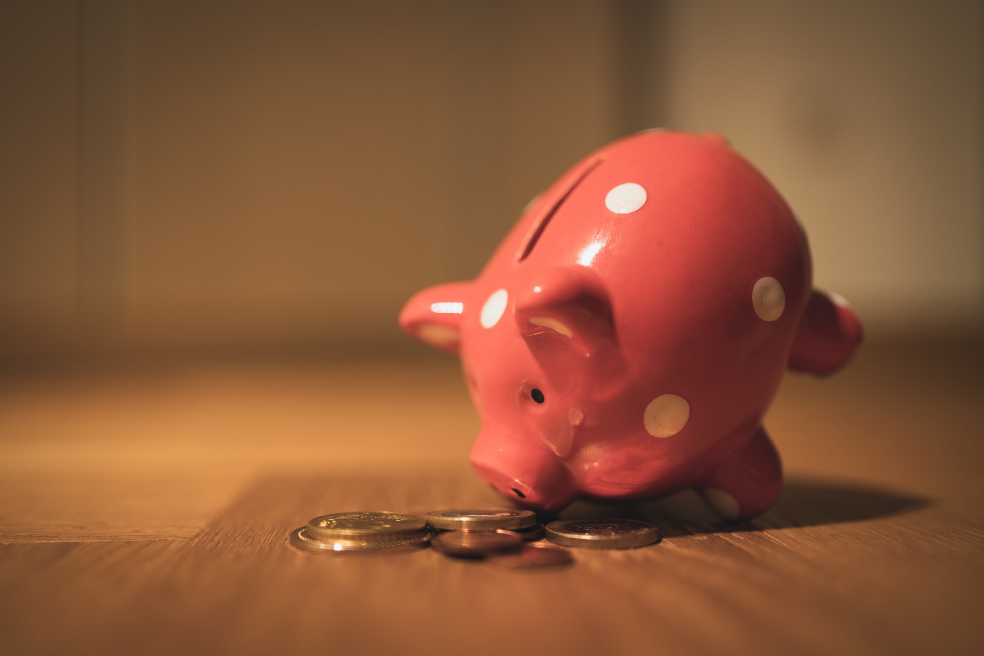 Your value - piggybank with polka dots tipped forward on a wooden table with coins in front on its nose