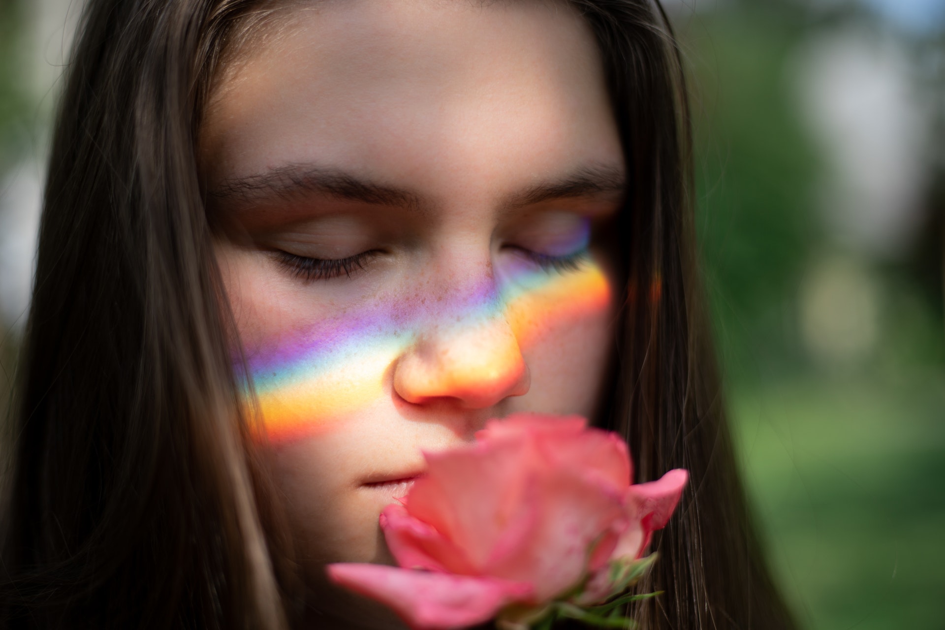Embrace your intuition - woman with a rainbow reflected on her face smelling a pink rose