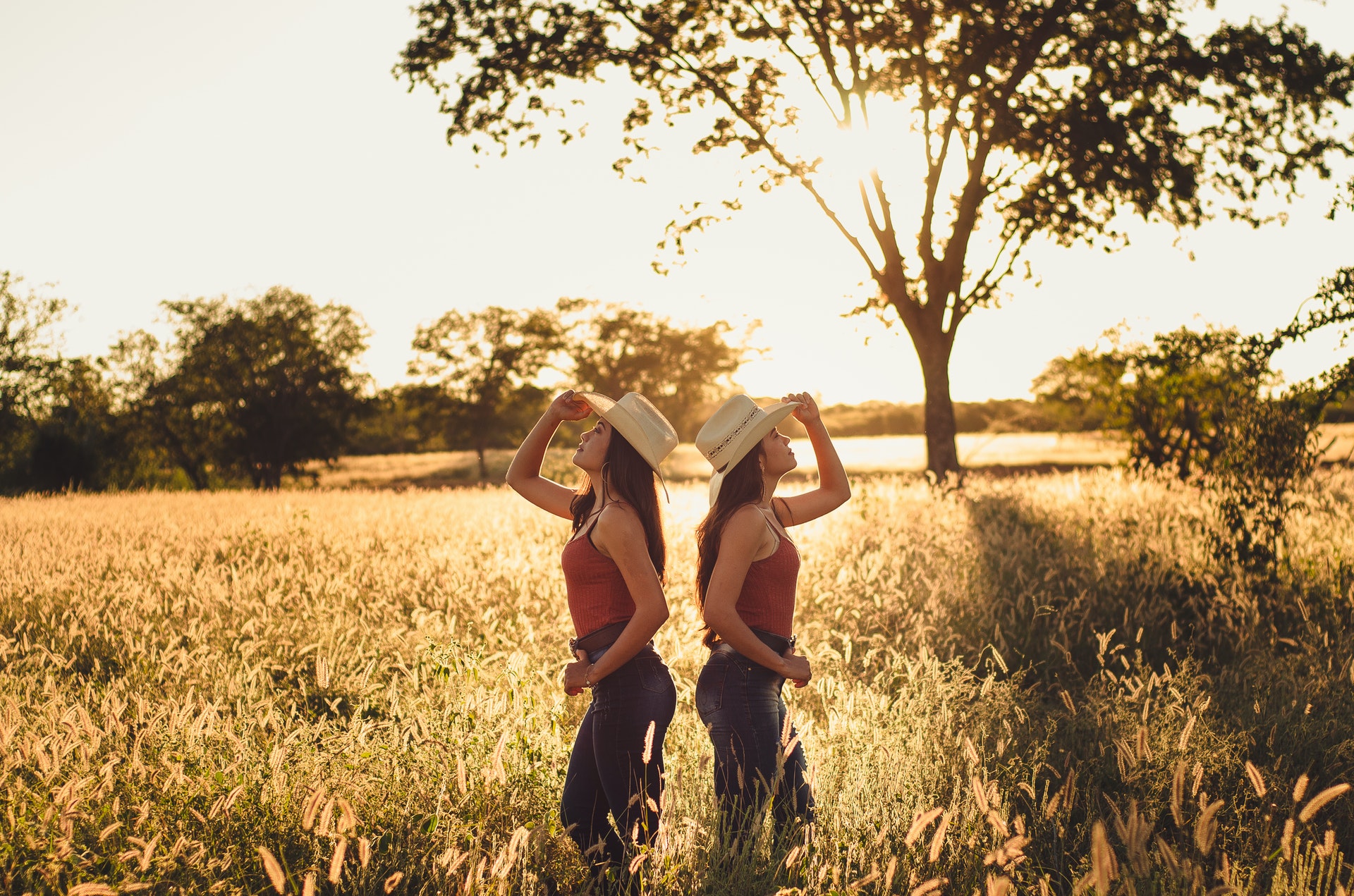 Soul vs ego - twin adult women in a sunny field back to back wearing sun hats and looking in opposite directions