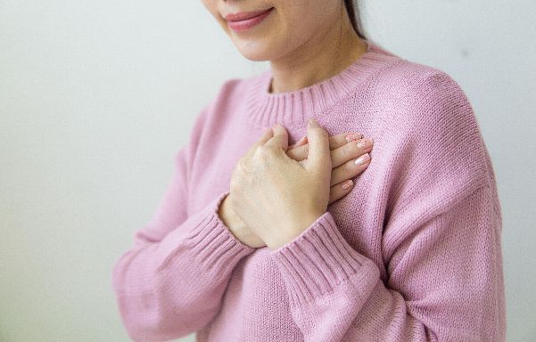 Why the Theta Brainwave? Woman in a pale pink sweater with hands crossed on her heart.