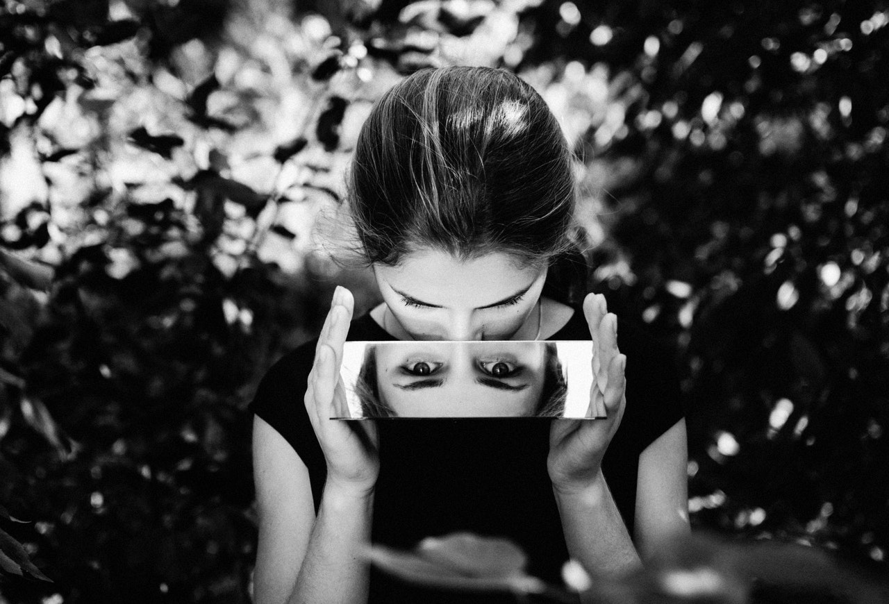 know thyself meaning - young woman in black tshirt looking down into a mirror so her eyes are reflected. Image is black and white.